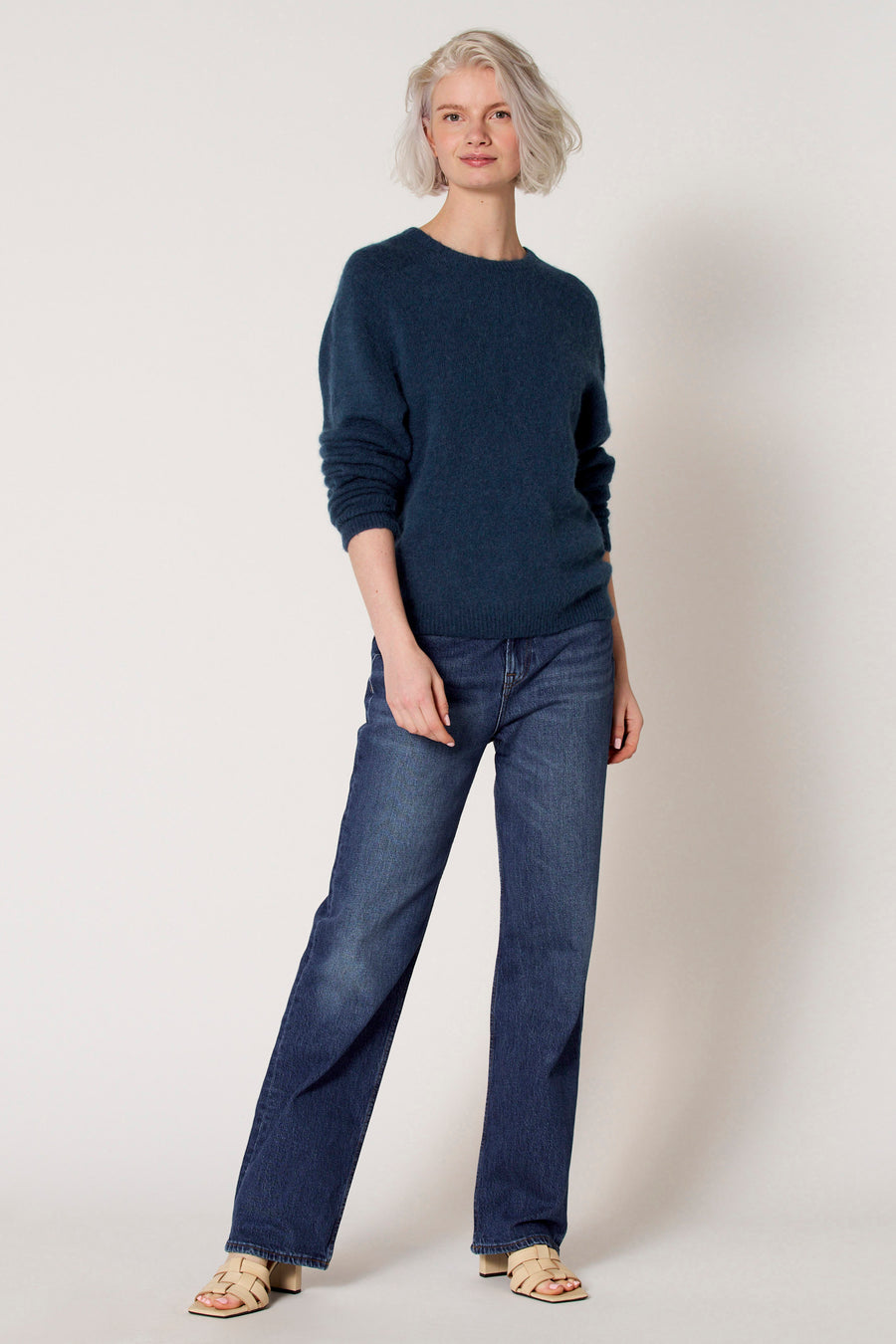 Blauwe trui met ronde hals van Clouds of Fashion, gecombineerd met donkerblauwe jeans en beige sandalen.
