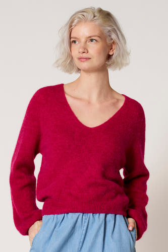 Roze V-hals trui van Clouds of Fashion, gedragen met een blauwe rok en een effen achtergrond.
