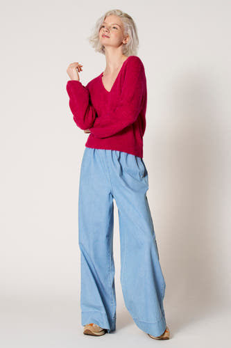 Roze V-hals trui van Clouds of Fashion, gecombineerd met wijde lichtblauwe broek en bruine schoenen.
