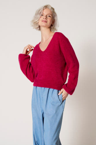 Roze trui met V-hals van Clouds of Fashion, gedragen met lichtblauwe broek en een hand in de zak.