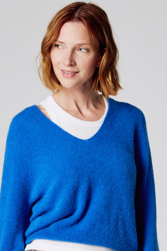 T-shirt bleu à col V de Clouds of Fashion, en tissu doux, porté sur un chemisier blanc.