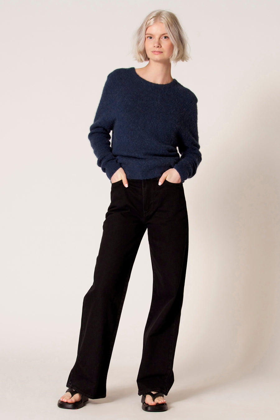 Blauwe trui met ronde hals van Clouds of Fashion, gedragen met zwarte broek en sandalen.