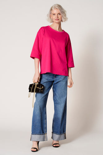 Vrouw in roze shirt, wijde jeans en zwarte sandalen met handtas.
