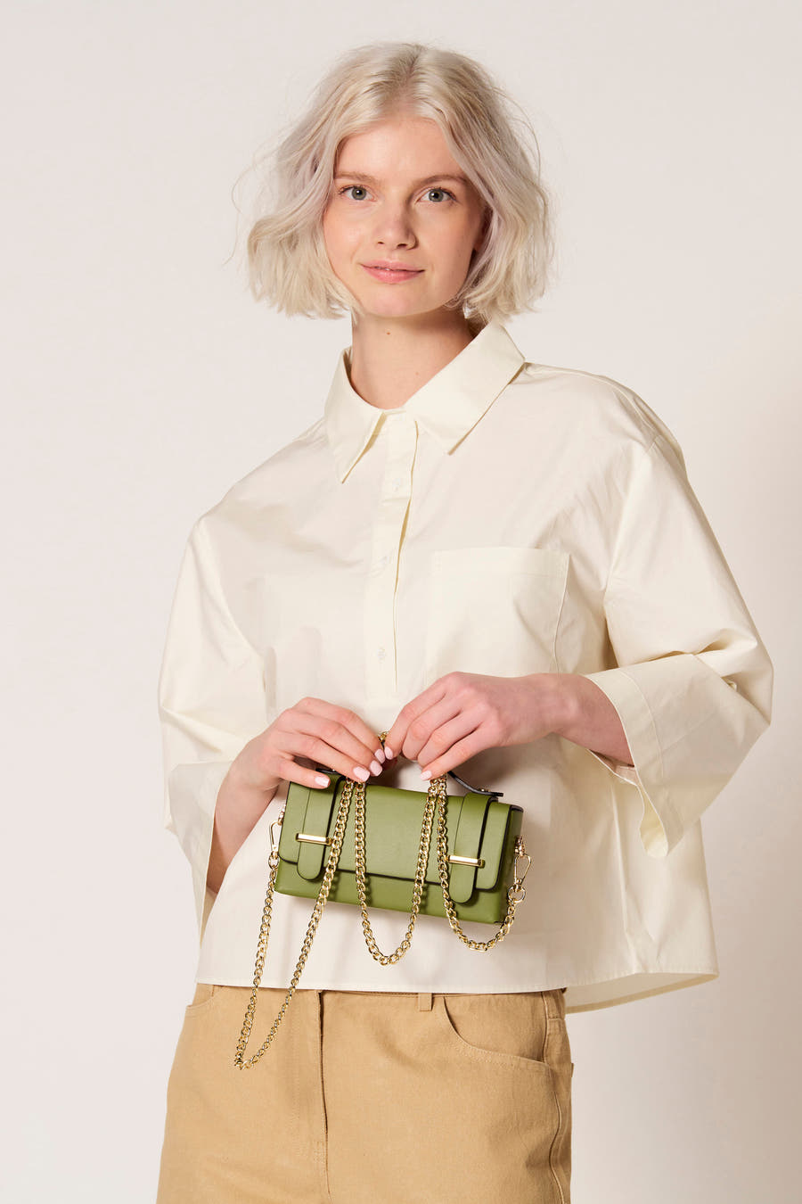 Groene handtas van Clouds of Fashion met gouden ketting, gecombineerd met een beige broek en crèmekleurige blouse.
