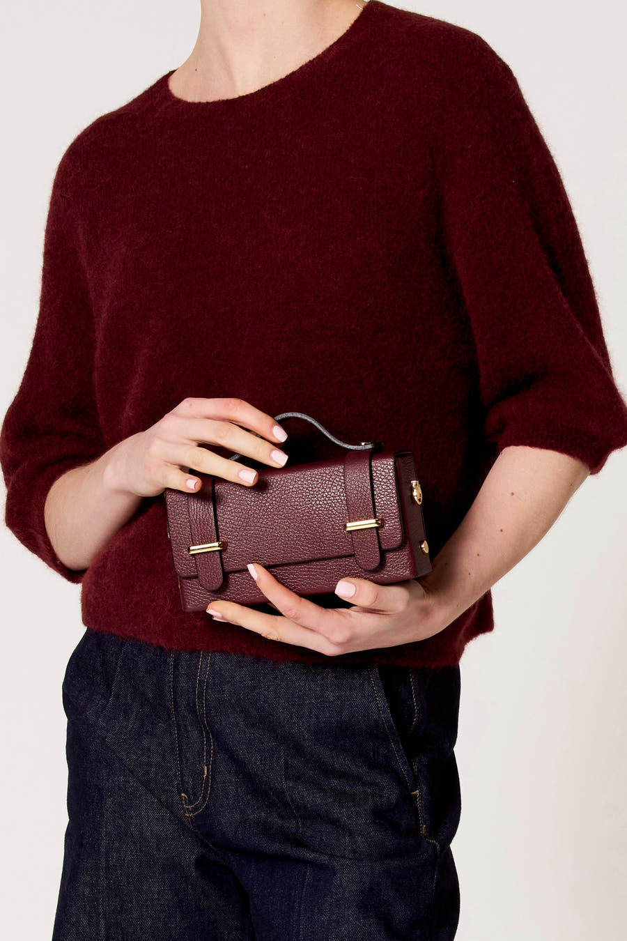 Bordeaux handtas van Clouds of Fashion, met gouden details, gedragen met een bordeaux trui en donkere jeans.
