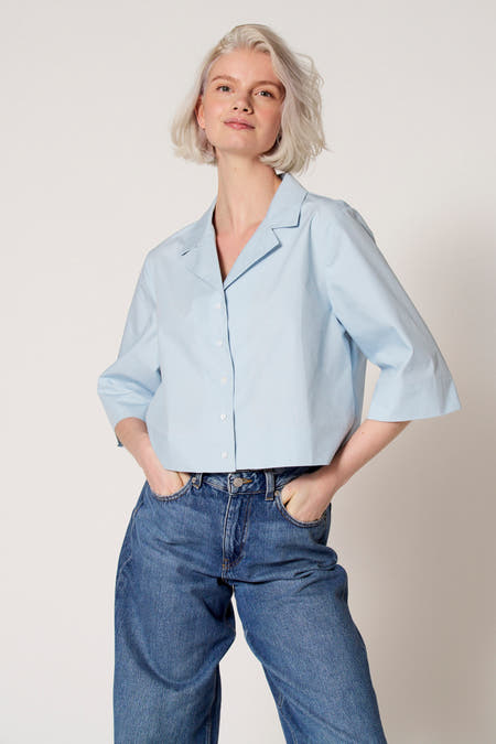 Chemisier bleu à manches trois-quarts de Clouds of Fashion, porté avec un jean à jambes larges.