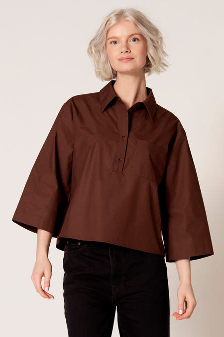 Chemisier marron à manches trois-quarts de Clouds of Fashion, avec une fermeture boutonnée et une poche poitrine, combiné avec un jean noir.