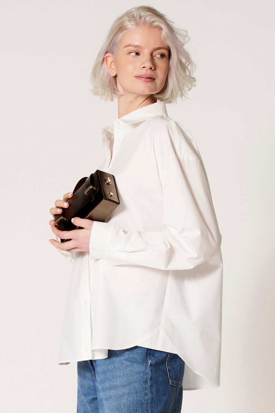 Witte blouse met lange mouwen van Clouds of Fashion, gedragen met blauwe jeans en een bruine handtas.