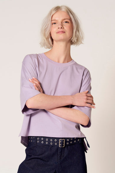 T-shirt violet à manches courtes de Clouds of Fashion, coupe ample et porté avec un pantalon bleu foncé à ceinture.