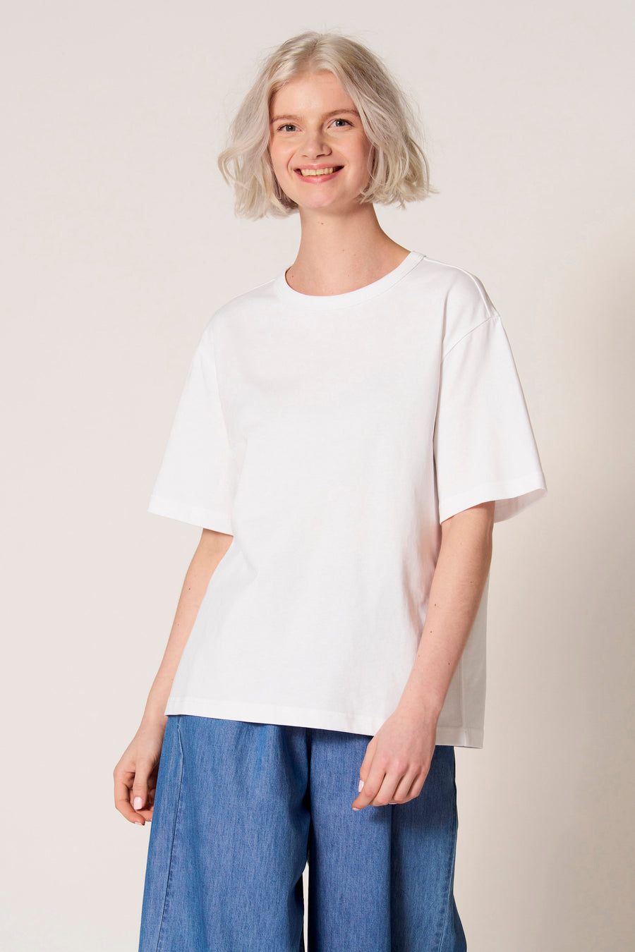 T-shirt blanc à manches courtes de Clouds of Fashion, avec une coupe ample et associé à un pantalon bleu.
