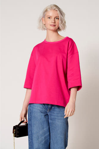 T-shirt rose à manches courtes de Clouds of Fashion, avec une coupe décontractée, associé à un jean bleu et un sac à main noir.