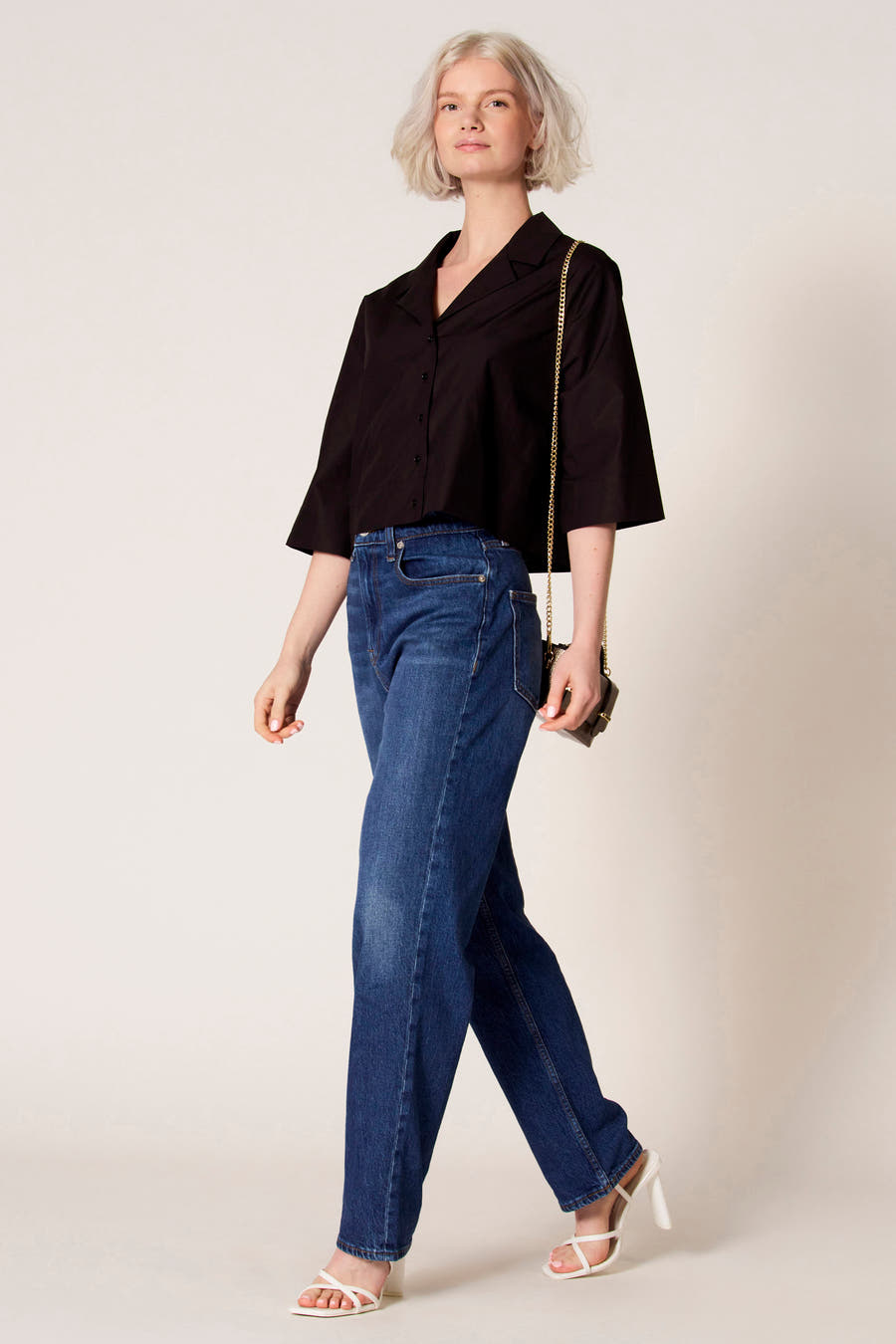 Zwarte blouse met driekwart mouwen van Clouds of Fashion, gecombineerd met een donkerblauwe jeans en witte hakken met bandjes.