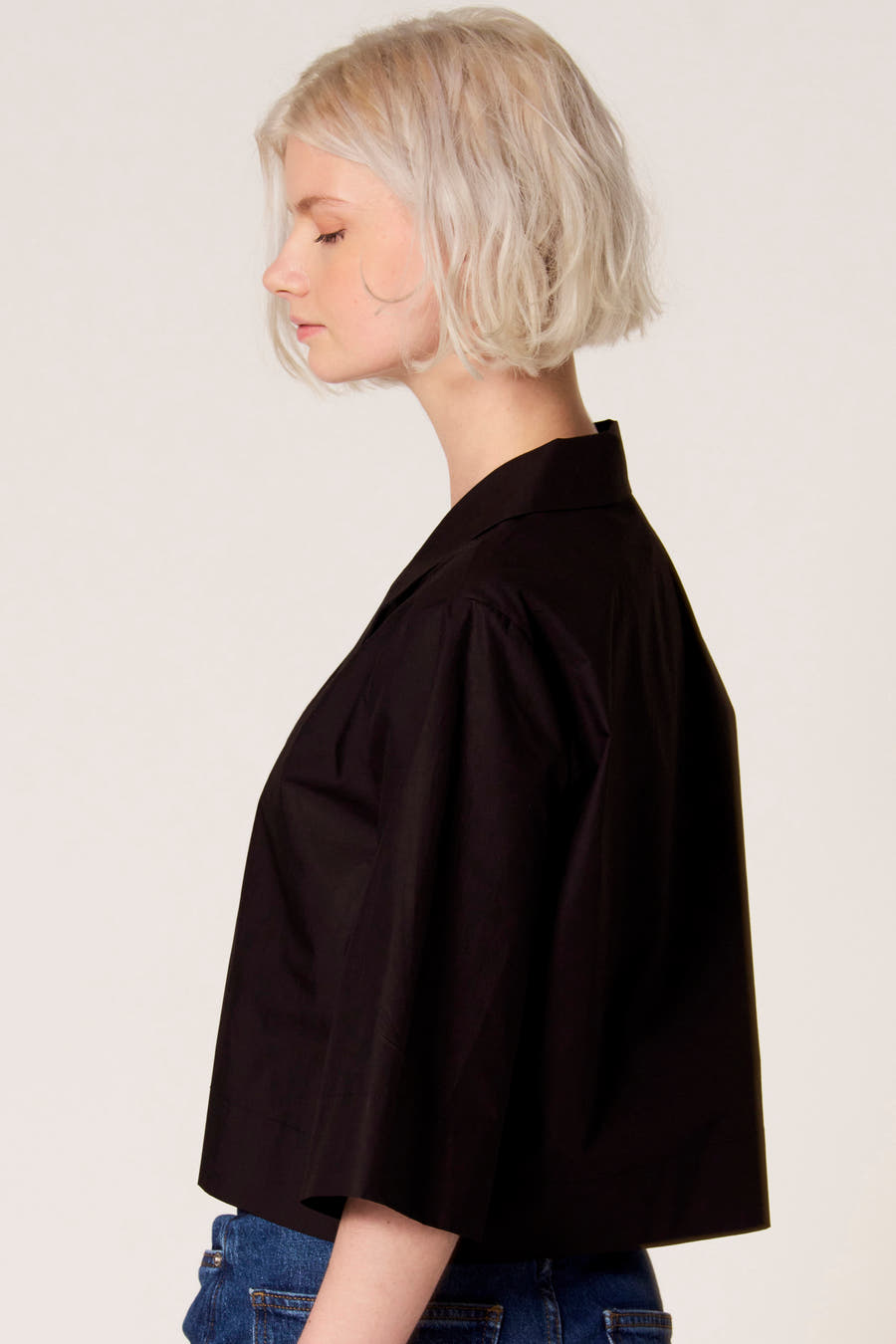 Zwarte blouse van Clouds of Fashion, in zijaanzicht gedragen met een blauwe jeans.
