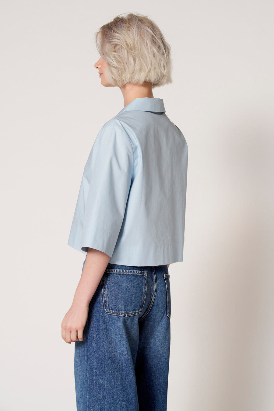 Blauwe blouse met driekwart mouwen van Clouds of Fashion, gedragen met een jeans met wijde pijpen, gezien van achteren.
