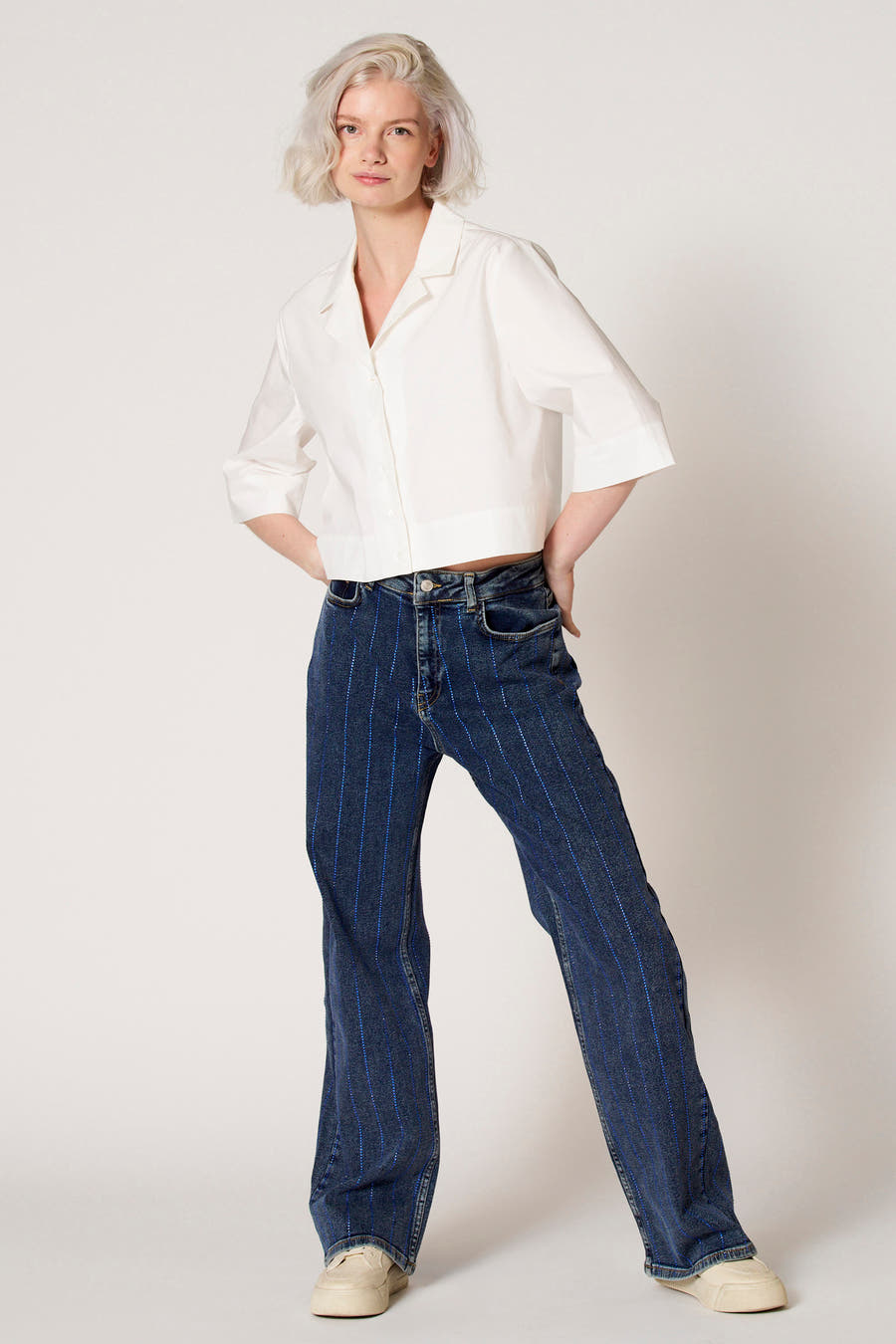 Blouse blanche de Clouds of Fashion, avec des manches trois-quarts, portée avec des jeans rayés bleus.