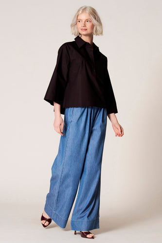 Blouse noire à manches trois-quarts de Clouds of Fashion, coupe décontractée, portée avec des jeans larges et des talons.