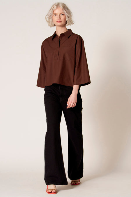 Blouse brune de Clouds of Fashion, avec un col, une poche poitrine et des manches trois quarts, associée à des pantalons noirs et des chaussures ouvertes.