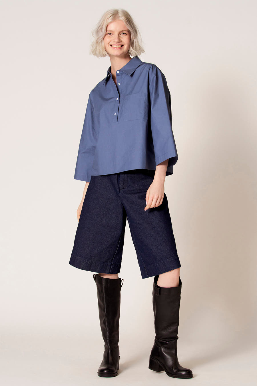 Blauwe blouse met driekwart mouwen van Clouds of Fashion, met een borstzak en gedragen met donkerblauwe culottes en zwarte laarzen.
