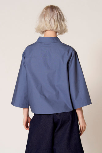 Blauwe blouse met driekwart mouwen van Clouds of Fashion, gezien vanaf de achterkant, gecombineerd met een donkerblauwe broek.
