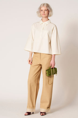 Witte blouse met driekwart mouwen van Clouds of Fashion, met borstzak en gedragen met bruine broek en groene handtas.
