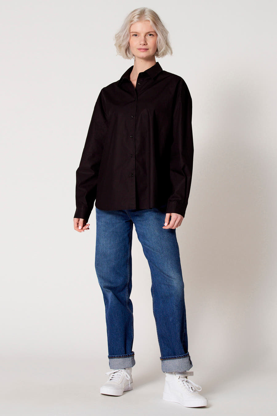 Blouse noire à manches longues de Clouds of Fashion, portée avec des jeans et des baskets blanches.