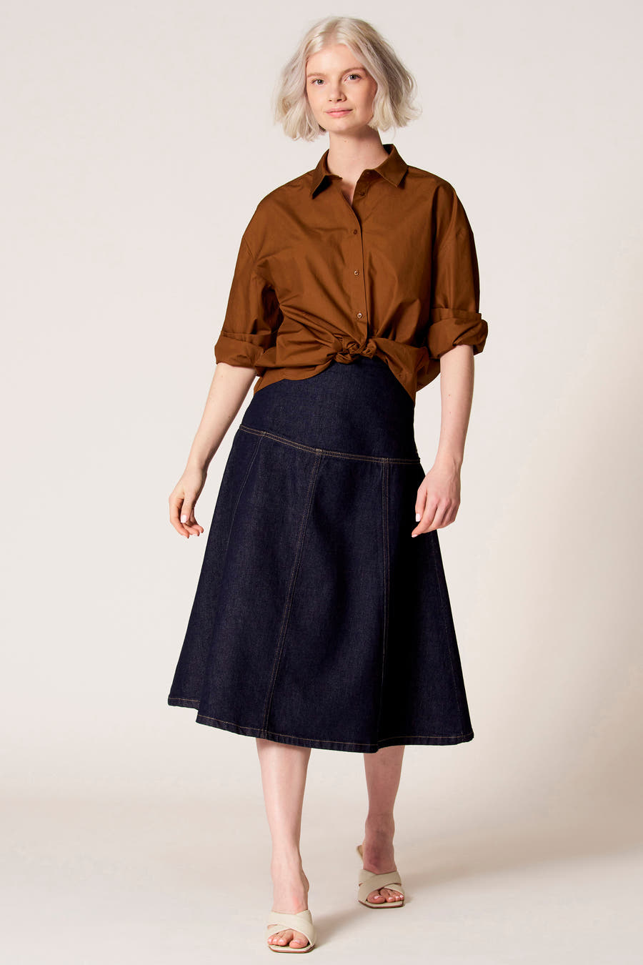 Blouse brune à longues manches de Clouds of Fashion, boutonnée devant, portée avec une jupe en denim bleu marine.