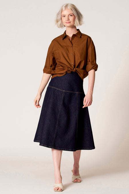 Blouse brune à longues manches de Clouds of Fashion, boutonnée devant, portée avec une jupe en denim bleu marine.