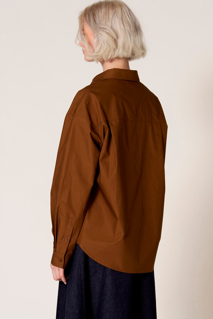 Bruine blouse met lange mouwen van Clouds of Fashion, met een klassieke kraag en lange mouwen gedragen met een donkerblauwe rok.
