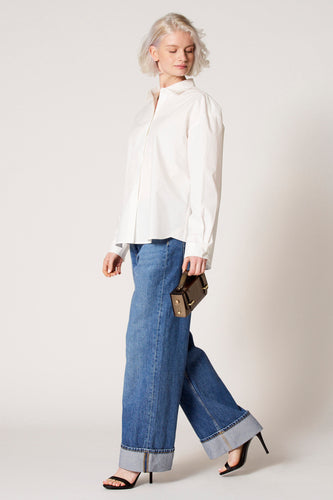 Blouse blanche à longues manches de Clouds of Fashion, portée avec des jeans larges et des talons noirs, en vue latérale.