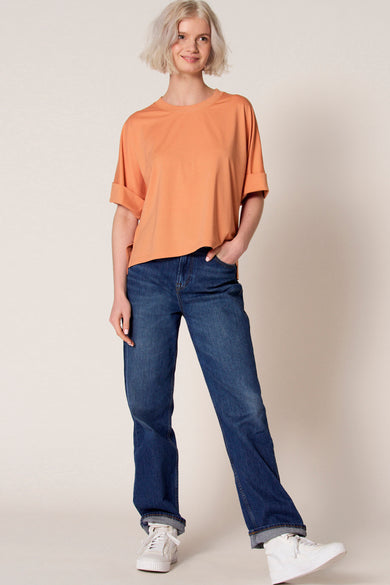 Oranje T-shirt met korte mouwen van Clouds of Fashion, met opgerolde mouwen, gecombineerd met een donkere jeans en witte sneakers.