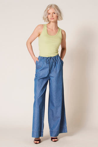 Groene singlet van Clouds of Fashion, gedragen met blauwe, wijde broek en donkerrode sandalen.