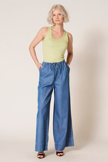 Groene singlet van Clouds of Fashion, gedragen met blauwe, wijde broek en donkerrode sandalen.