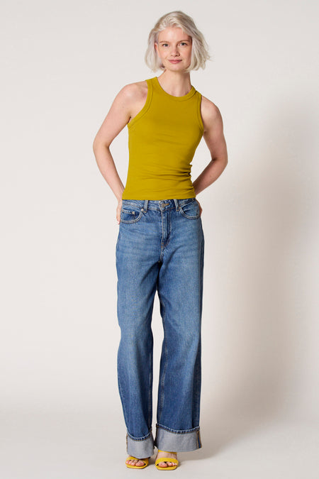 Groene singlet van Clouds of Fashion, gedragen met losse jeans en gele sandalen.