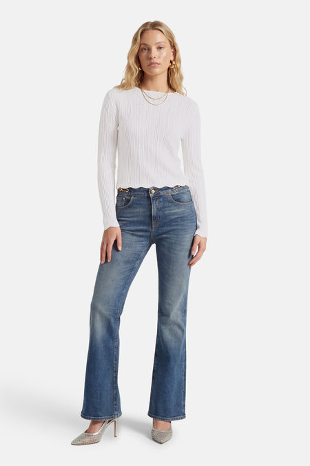 Wit T-shirt met lange mouwen van HAILYS, met een gehaakt patroon, gecombineerd met blauwe jeans en zilveren hakken.

