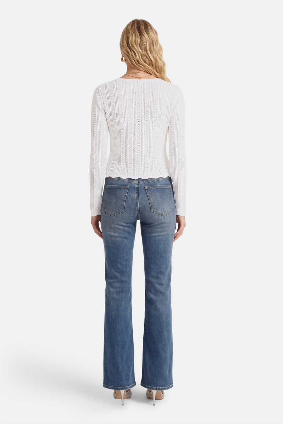 Witte T-shirt met lange mouwen van HAILYS, met een opengebreide textuur en een geschulpte zoom, gecombineerd met blauwe jeans en hakken.