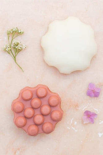 Conditionneur barre avec melon doux de WONDR CARE, à côté de fleurs et de pétales sur un fond rose.