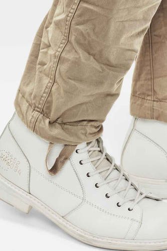 Jean cargo beige de G-Star RAW, avec des poches à glissière et des coutures visibles, associé à des bottes en cuir blanches.