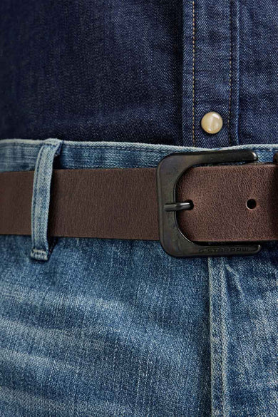 Ceinture brune de G-Star RAW, avec une boucle métallique, portée sur un jean bleu et un chemisier en denim.