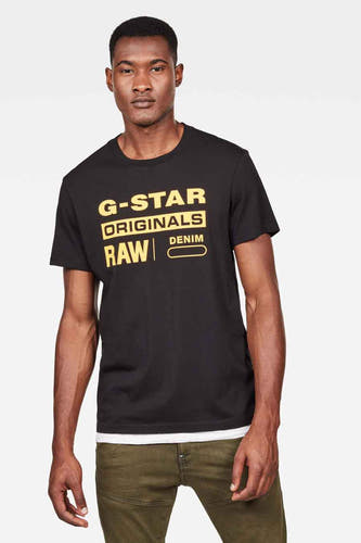 Zwart T-shirt van G-Star RAW met gele merklogo's en gedragen met een groene broek.
