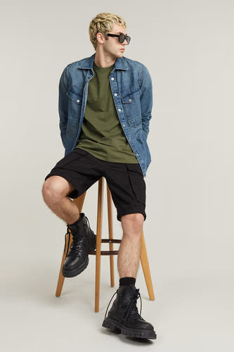 T-shirt vert de G-Star RAW, porté sous un gilet en denim et associé à des shorts noirs et des bottes.
