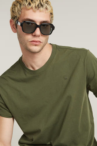 T-shirt vert de G-Star RAW, avec des manches courtes et un col rond, porté avec une chaîne en argent et des lunettes de soleil noires.