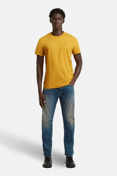 Geel T-shirt met korte mouwen van G-Star RAW, gedragen met blauwe jeans en zwarte schoenen.