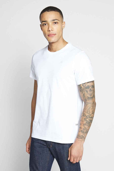 T-shirt blanc de G-Star RAW, dos nu, avec un tatouage sur le bras gauche et des jeans bleus.