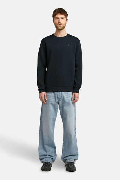 Blauwe sweater met ronde hals van G-Star RAW, gedragen met wijde jeans en zwarte sneakers.
