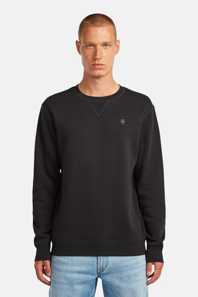 Pull-over gris à col rond de G-Star RAW, avec un petit logo sur la poitrine et porté avec un jean bleu.
