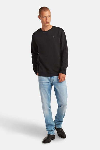 Pull-over gris de G-Star RAW, porté avec des jeans bleus et des chaussures noires.
