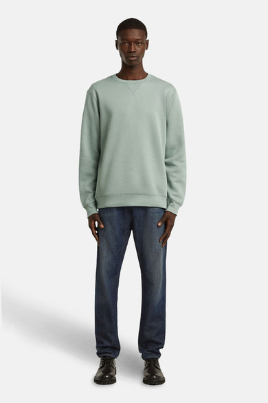 Pull-over vert vert avec col rond de G-Star RAW, associé à des jeans foncés et des chaussures noires.