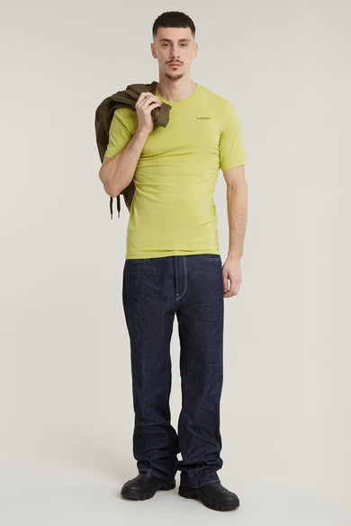 Geel T-shirt met korte mouwen van G-Star RAW, met een jas over de schouder, gecombineerd met donkere jeans en zwarte schoenen.
