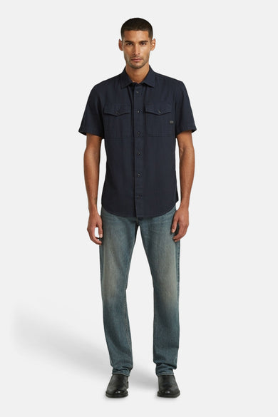 Chemise bleue à manches courtes de G-Star RAW, avec deux poches poitrine et portée avec un jean et des chaussures noires.