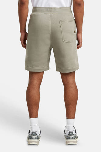 Grijze sweat short van G-Star RAW, achteraanzicht met opgestikte achterzak en merklabel, gedragen met witte sokken en sneakers.